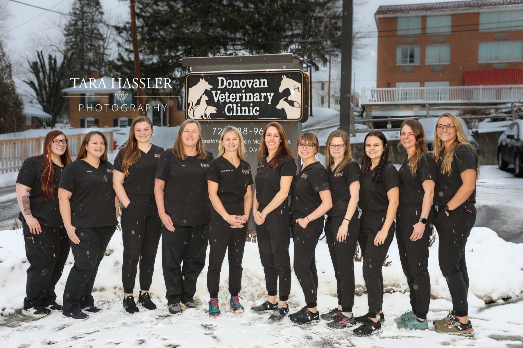 The Donovan Veterinary Clinic team, thirteen women in black scrubs, standing in the snow in front of the clinic's sign on Loyalhanna Street